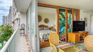 A balcony with a bed, a TV, wicker furniture, and a view of the ocean. - Pool Access, 1 Mi to Makaha Beach! Ocean-view Unit (Waianae)