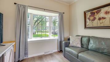 A room with a window, a grey leather sofa, a framed floral artwork, and a wooden cabinet.
