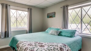 A bedroom with a bed, two windows, a painting on the wall, and a patterned throw blanket. - Fish, Swim + Relax: Modern Condo by Lake Huron! (Port Huron)