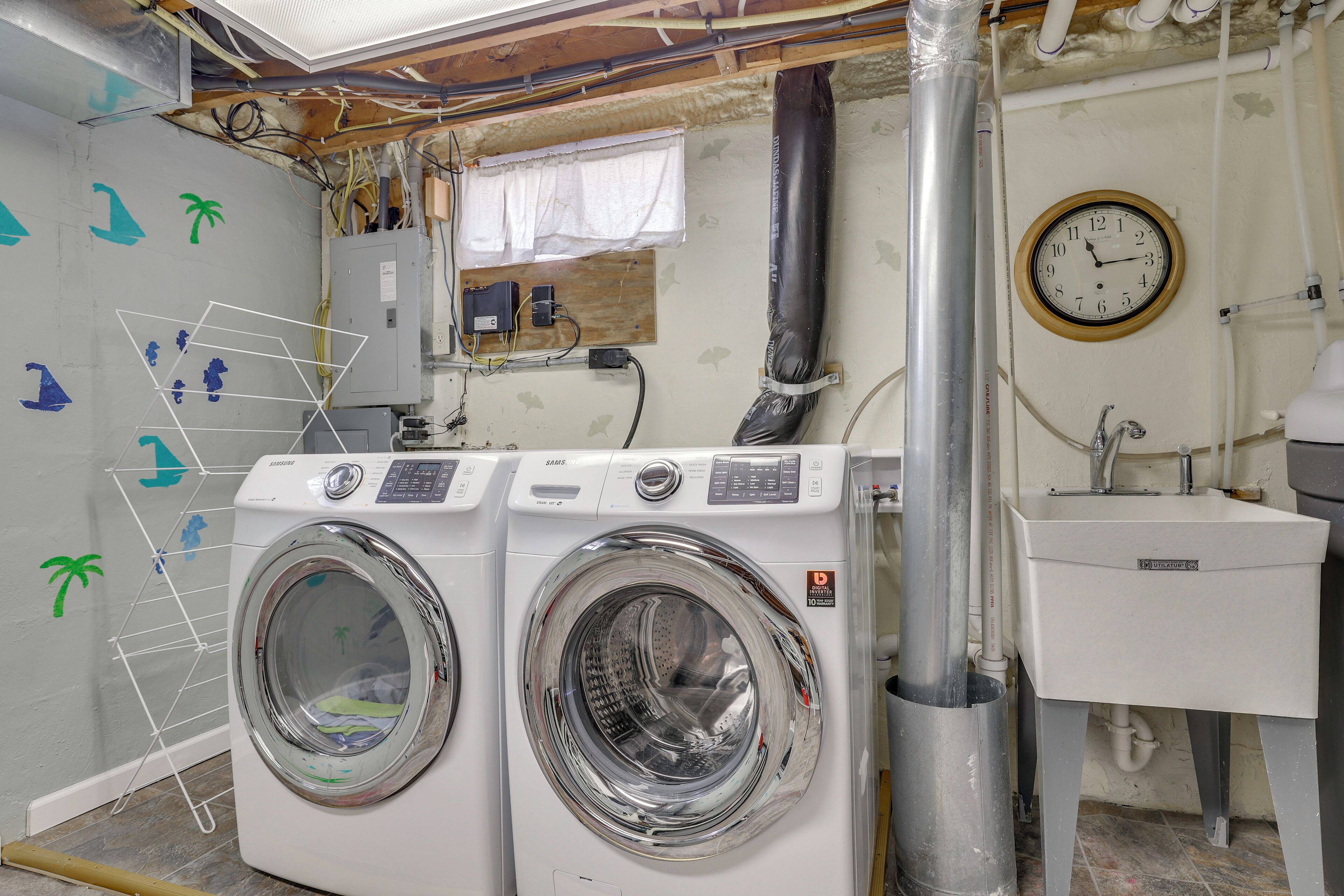 A laundry area with two front-loading washing machines, a sink, and a clock on the wall.