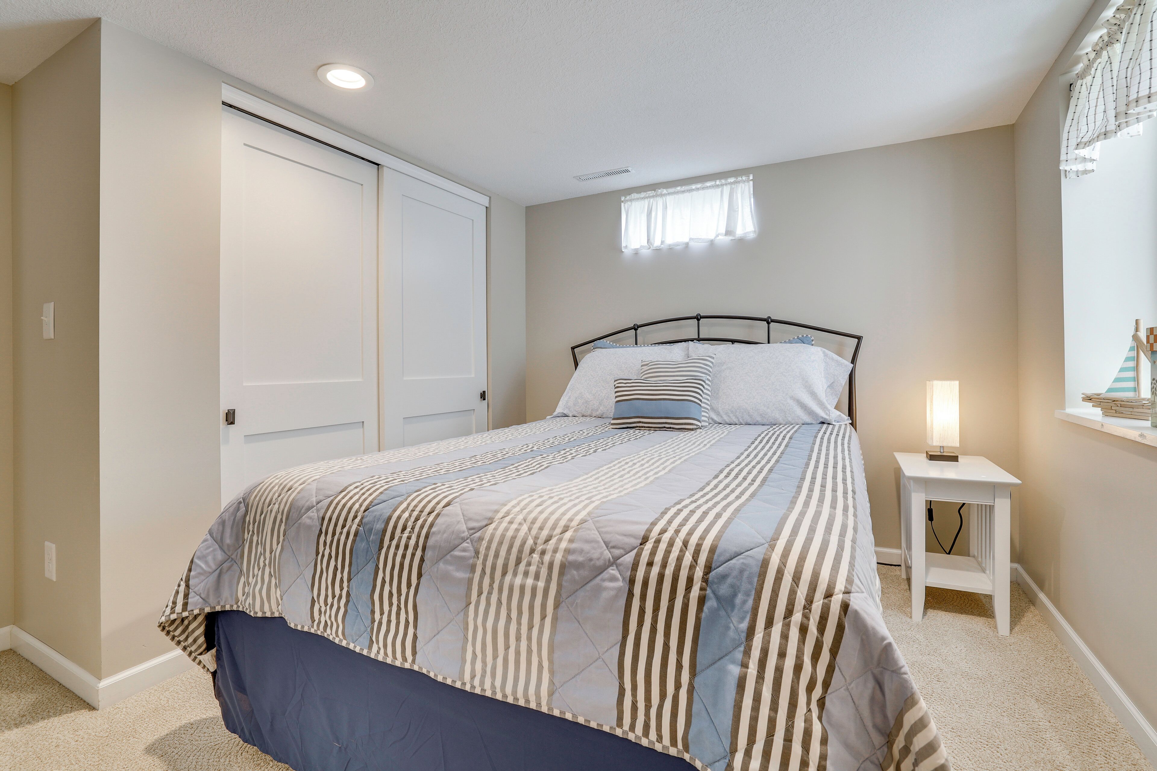 Un dormitorio con cama, mesita de noche con lámpara, ventana con cortinas y armario.