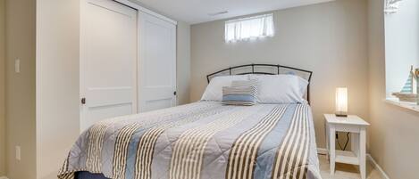 Un dormitorio con cama, mesita de noche con lámpara, ventana con cortinas y armario.
