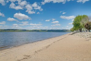 A beach with a clear sky, calm water, and a row of trees along the shore. - Steps to Lake Pepin, Beach! Charming Home w/ Patio (Lake City)