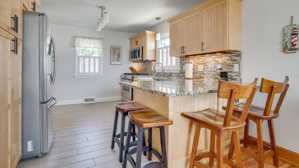 A kitchen with wooden cabinets, a granite countertop, a refrigerator, and bar stools.