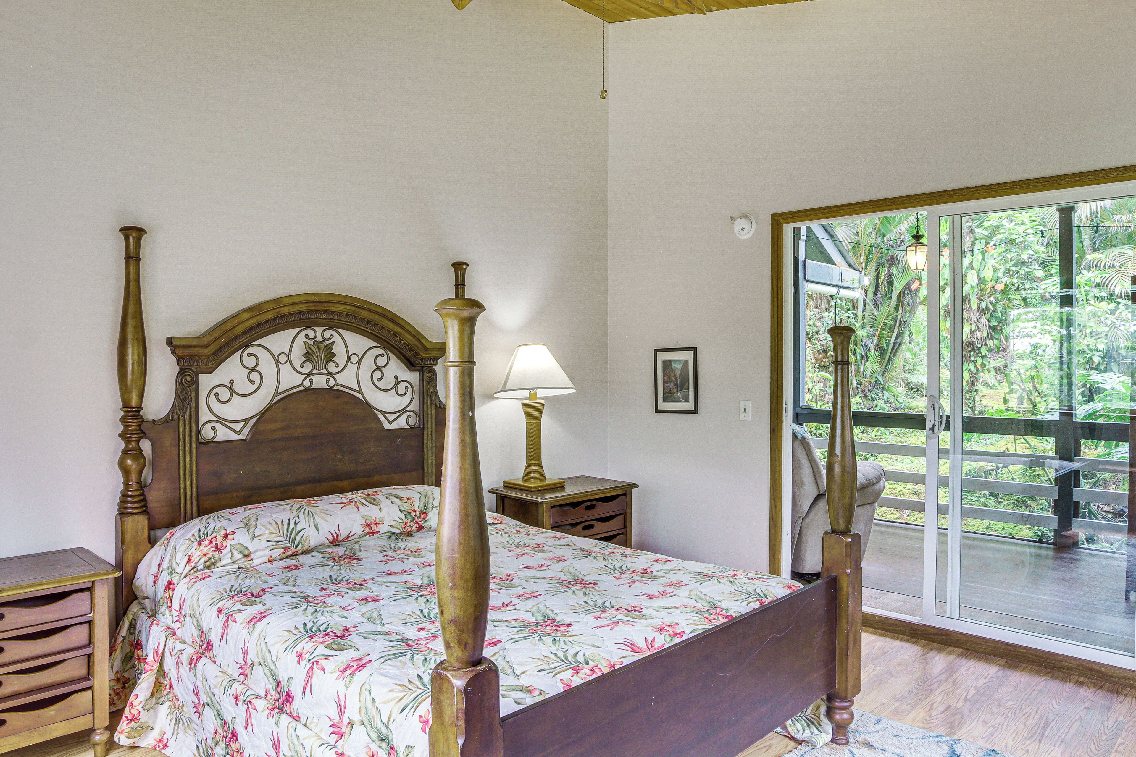 Un dormitorio con una cama de dos columnas de madera, una mesita de noche con lámpara y vistas a una terraza a través de una puerta de cristal.