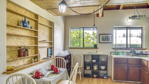 Una cucina con scaffali in legno, un tavolo da pranzo, sedie e una finestra che si affaccia sul verde.