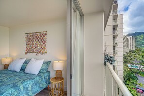 A balcony with a bed, a wall hanging, and a view of a cityscape. - Stay on Waianae Coast! Ocean-view Condo w/ Pools (Waianae)