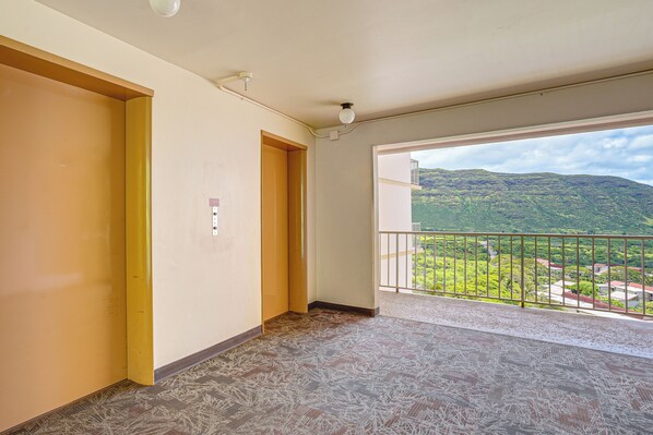 A room with a balcony, a door, and a view of a green landscape. - Stay on Waianae Coast! Ocean-view Condo w/ Pools (Waianae)