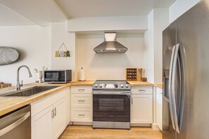 A modern kitchen with white cabinetry, stainless steel appliances, and a wooden countertop. - Stay on Waianae Coast! Ocean-view Condo w/ Pools (Waianae)