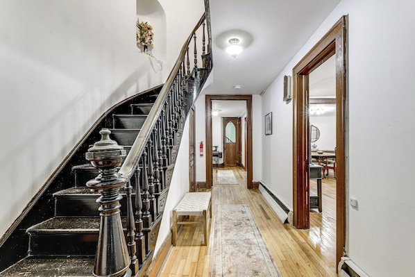 A staircase with ornate balusters, a wooden bench, and a rug leading to a dining area. - Historic Home 3 Mi to Middletown Main Street (Middletown)