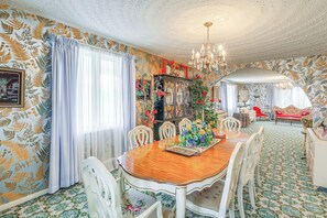 A dining room with a wooden table, white chairs, a chandelier, and patterned wallpaper.