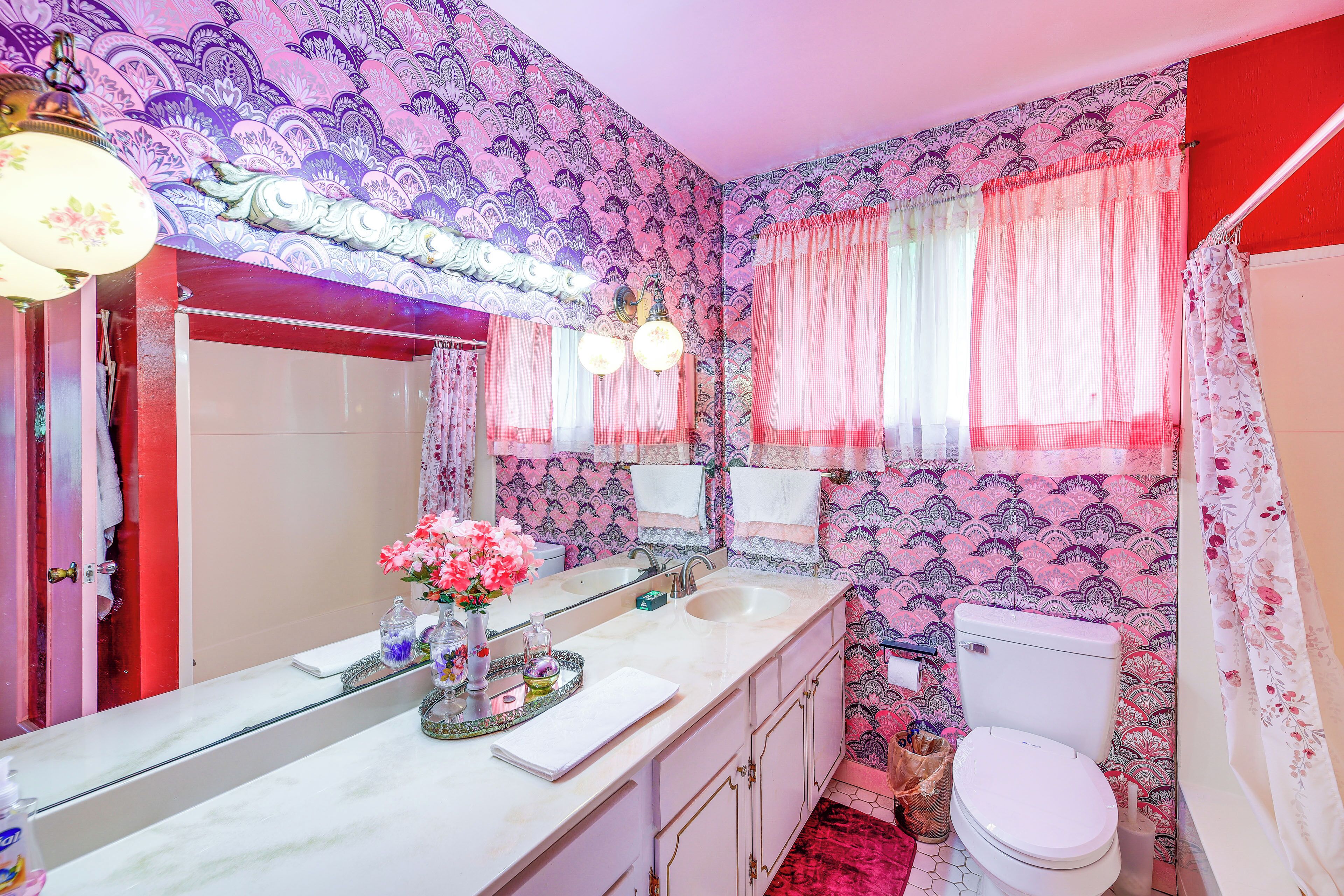 A bathroom with a large mirror, a sink, a toilet, and patterned wallpaper.