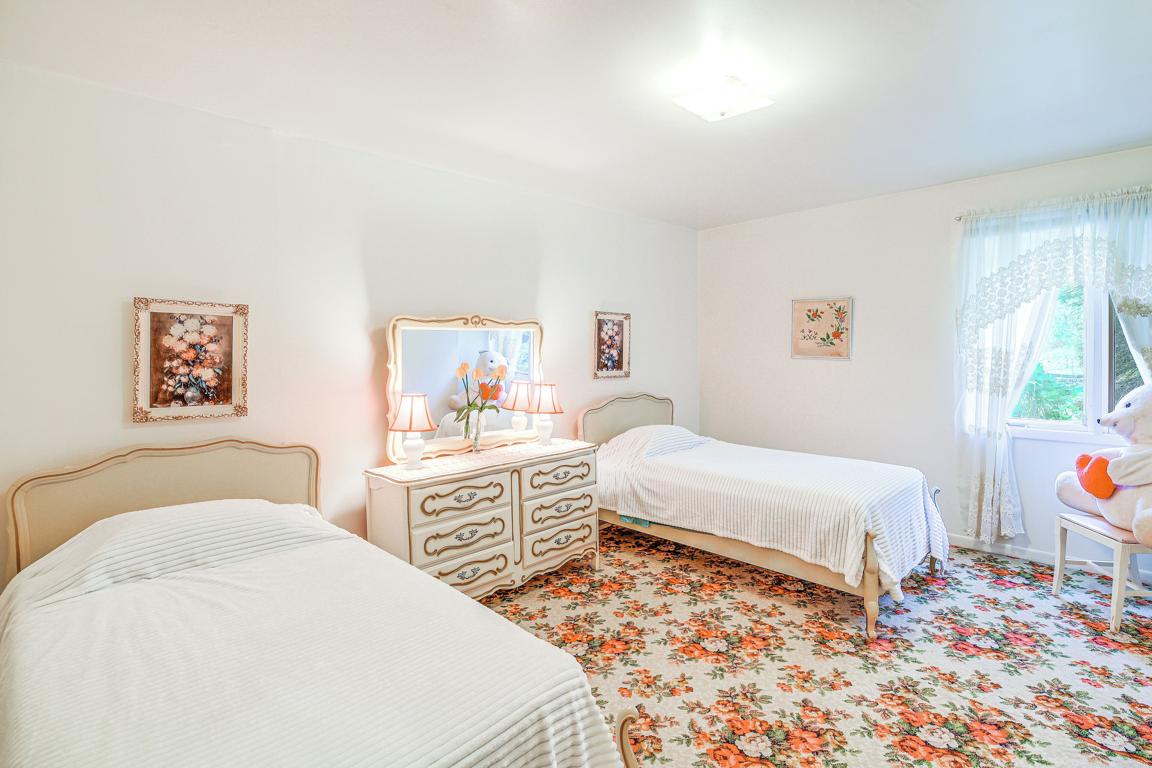A bedroom with two beds, a dresser, a mirror, and floral-patterned flooring.