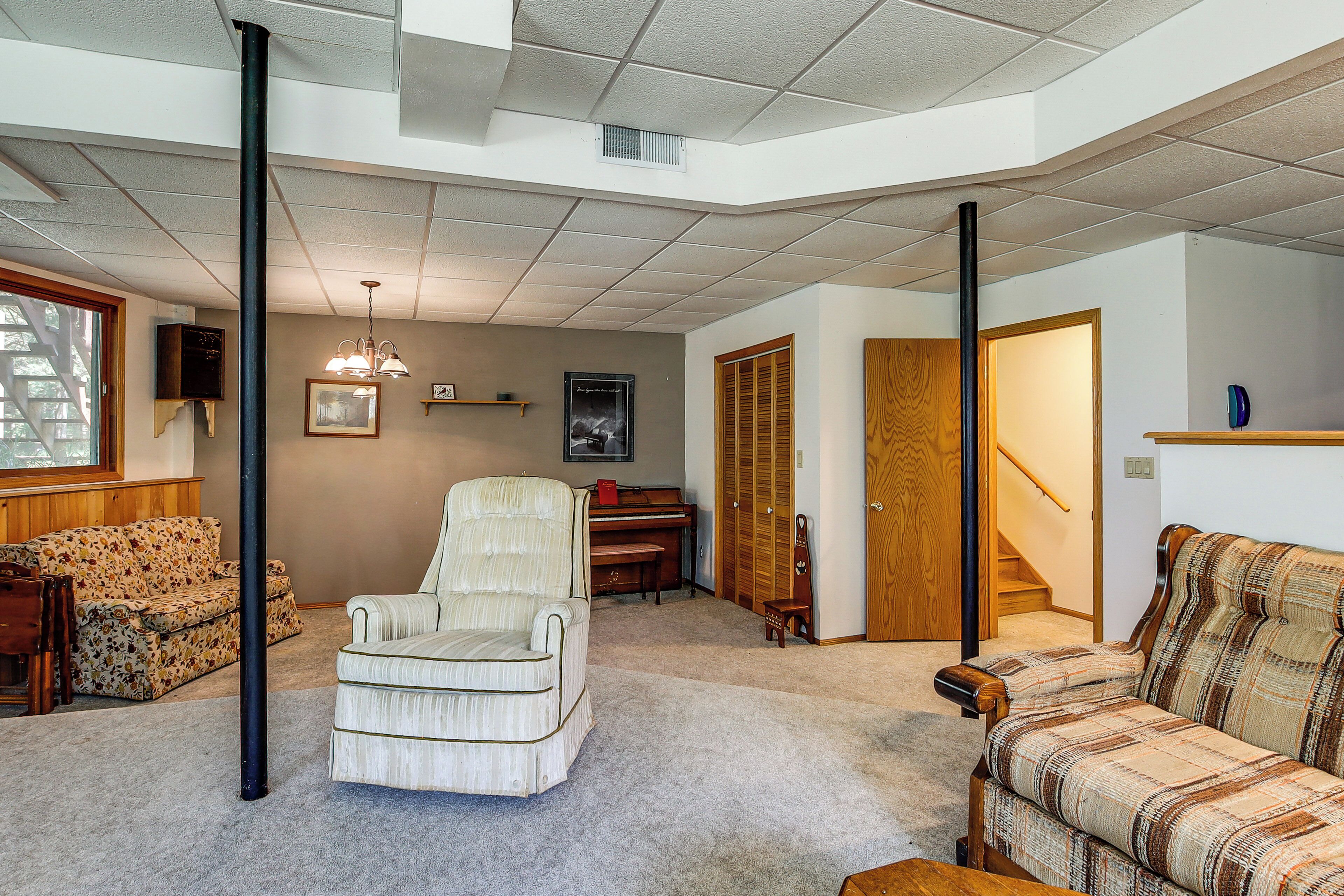 A living room with a piano, a sofa, a chair, and a staircase leading to another room.