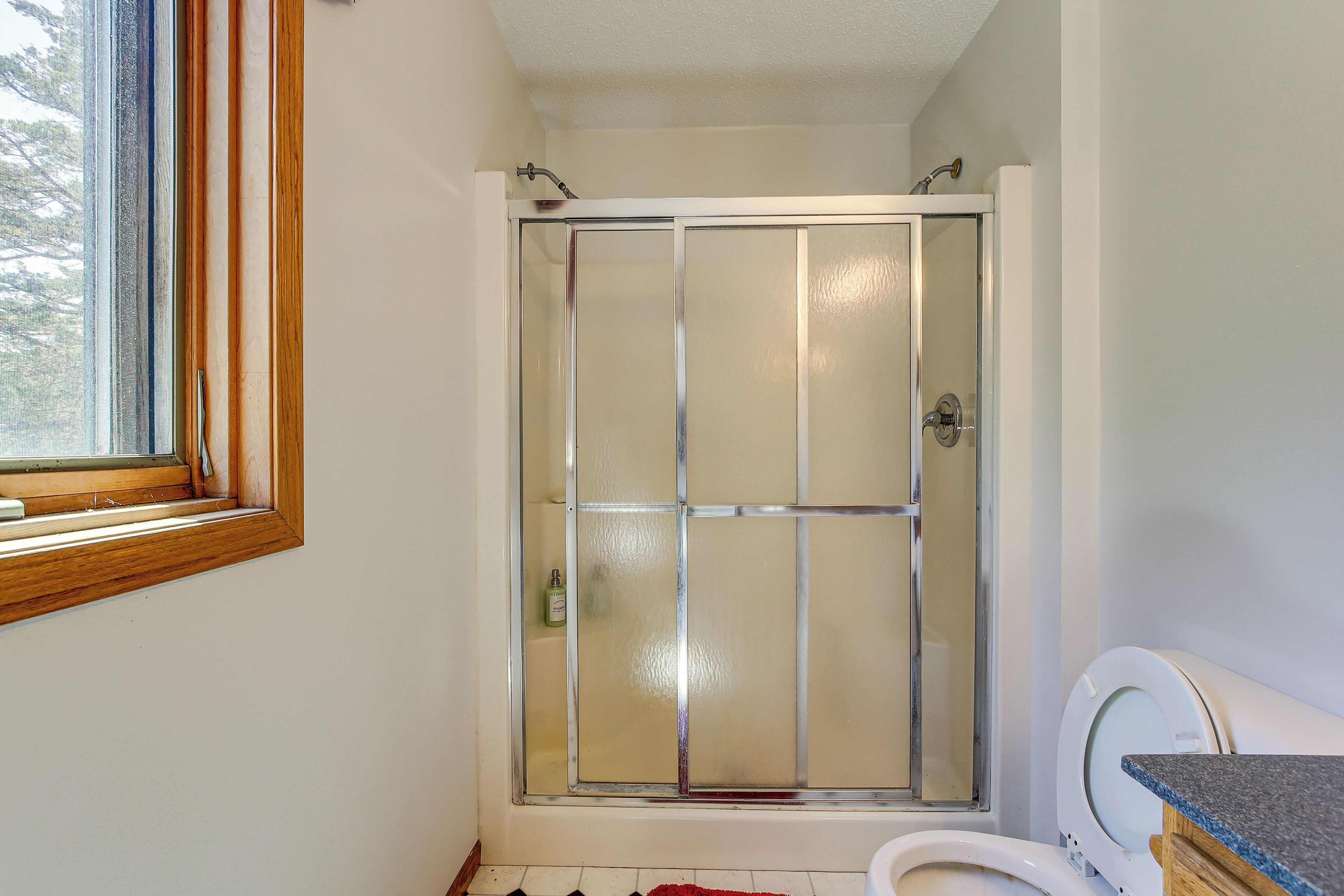 A bathroom with a glass shower enclosure, a toilet, and a window.