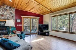 Un salon avec un mur en pierre, un plafond en bois, un téléviseur et de grandes fenêtres.