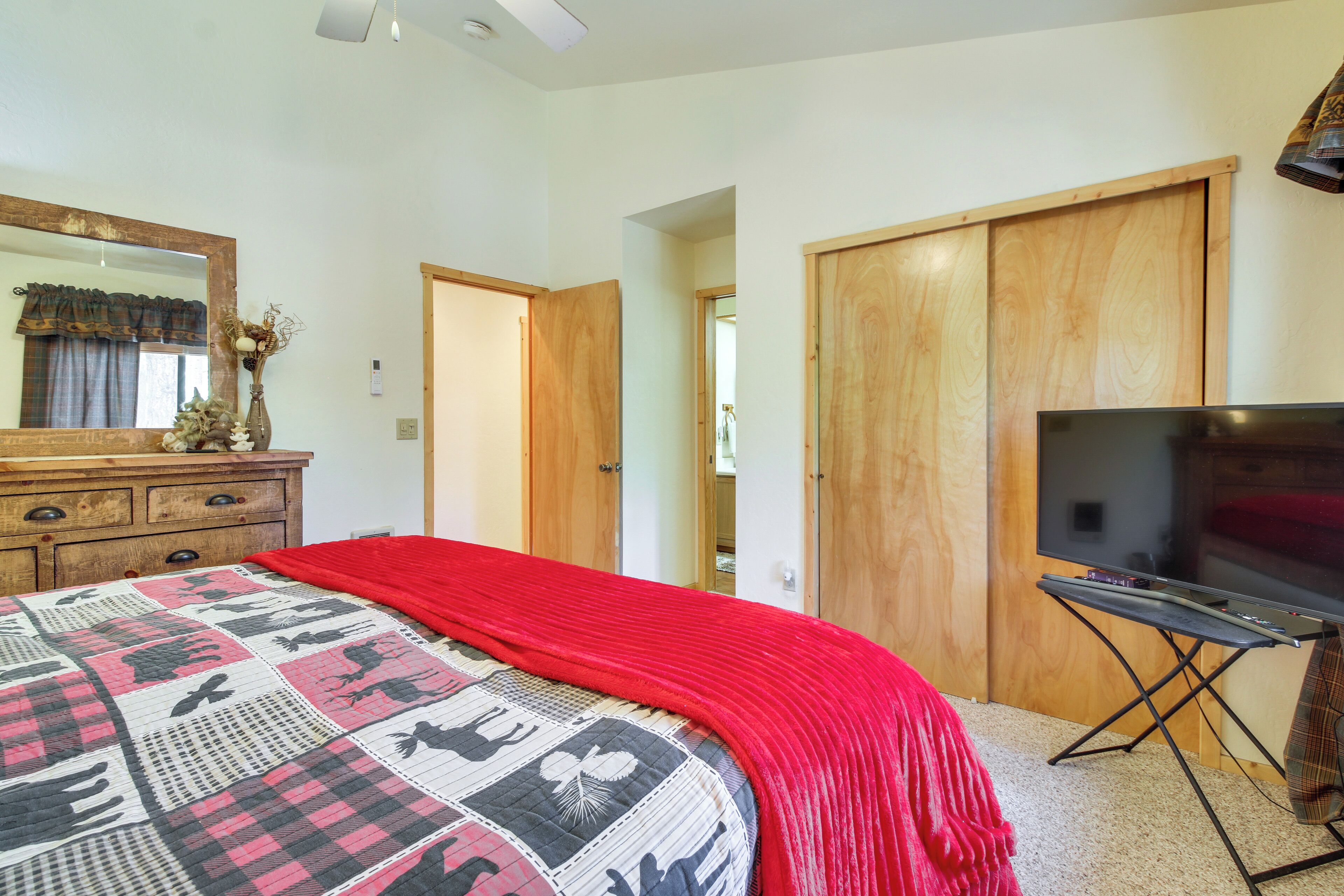 A bedroom with a large bed, a dresser, a TV on a stand, and a closet.