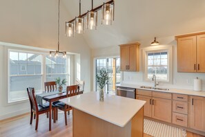 A kitchen with wooden cabinets, a white countertop, a dining table with chairs, and a hanging light fixture.