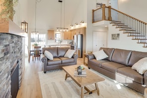 A spacious living area with a stone fireplace, leather sofas, a wooden coffee table, and a staircase leading to an upper level.