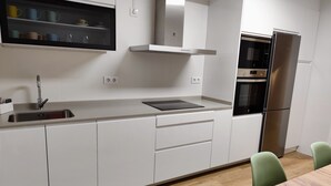 A modern kitchen with white cabinetry, a stainless steel refrigerator, a built-in oven, and a wooden dining table. - Cangas with charm (Cangas)