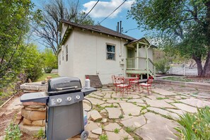 Ein Haus mit einer Steinterrasse, einem Grill und Gartenmöbeln.