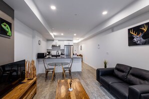 A modern kitchen with white cabinets, a stainless steel refrigerator, and a dining area with a round table and chairs. - Contemporary 1-Bedroom Suite in Regina | Metro 1827 Apartments (Regina)