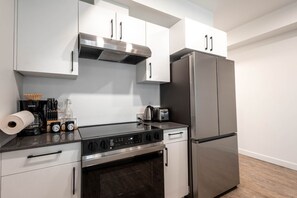 A modern kitchen with white cabinets, a stainless steel refrigerator, a stove, and a coffee maker. - Contemporary 1-Bedroom Suite in Regina | Metro 1827 Apartments (Regina)