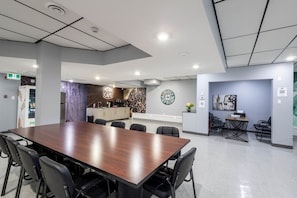 Una sala de reuniones moderna con una larga mesa, sillas, una kitchenette y un reloj en la pared.