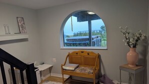 Um quarto com um banco de madeira, uma ampla janela em arco, uma pequena mesa com um vaso e uma escada.