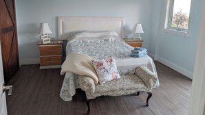 Quarto com cama, duas mesas de cabeceira, ventoinha no teto, ar condicionado, janela e porta.