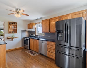 A modern kitchen with wooden cabinets, stainless steel appliances, and a ceiling fan.