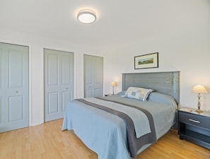 A bedroom with a bed, bedside tables, a nightstand, a picture on the wall, and three doors.