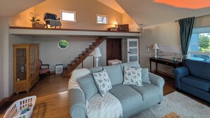Uma sala de estar estilo loft com escada, um sofá, uma poltrona azul, um armário e um aquário.
