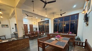 A spacious dining area with wooden tables and chairs, ceiling fans, and large windows. - Lap of Himalayas Resort Kausani (Kausani)