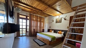 A room with a bed, wooden ceiling, a TV, a fan, a ladder, and a door. - Lap of Himalayas Resort Kausani (Kausani)