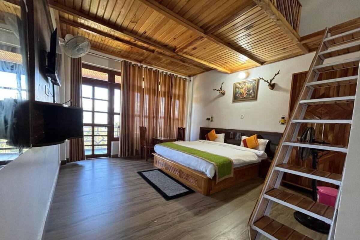 Una habitación con una cama, techo de madera, televisor, ventilador, escalera y una puerta.