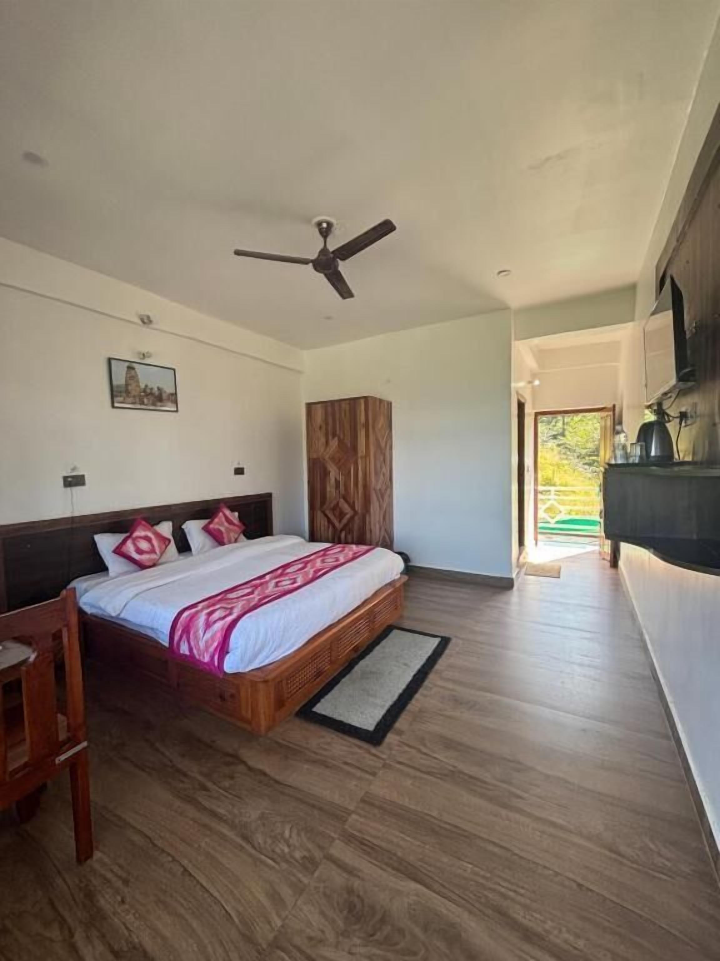 Une chambre à coucher avec un lit, un plancher en bois, un ventilateur de plafond et une vue sur l’extérieur.