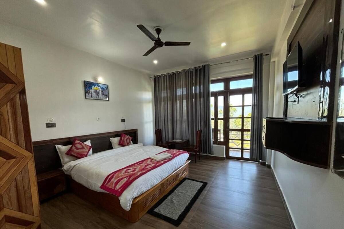 Un dormitorio con cama, ventilador de techo, televisor y ventana con cortinas.