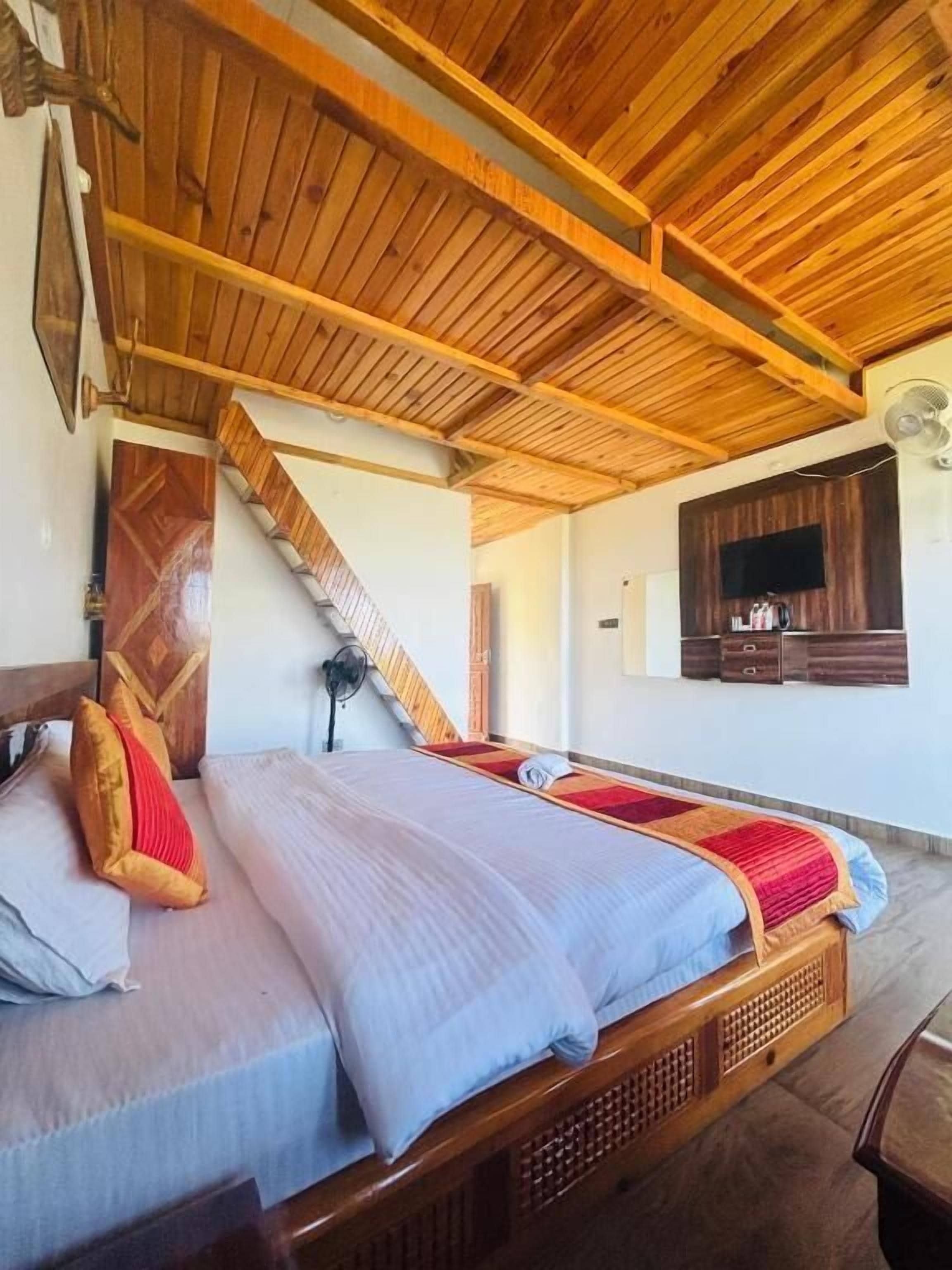Ein Schlafzimmer mit Holzbalkendecke, einem Bett mit Kissen, einem Fernseher an der Wand und einer Treppe.