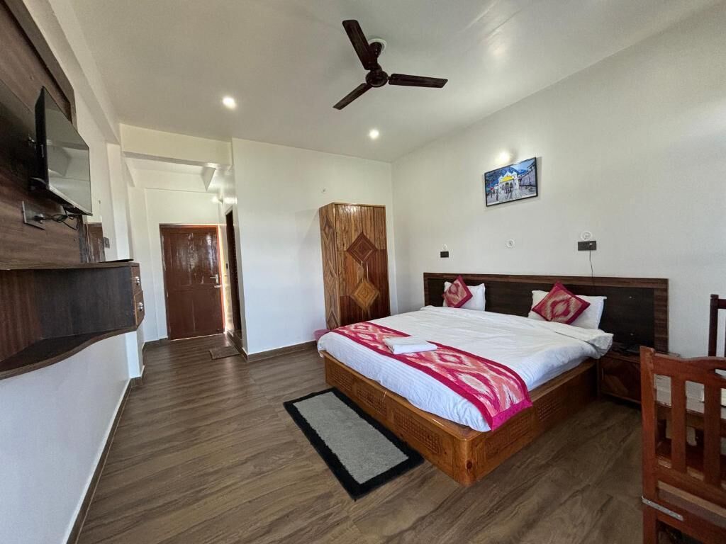 A bedroom with a wooden bed, a ceiling fan, a television, and a door leading to another room.