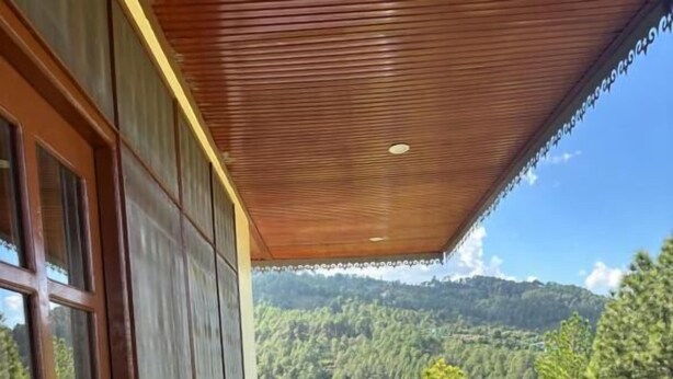A balcony with a wooden table and chairs, overlooking a forested landscape. - Lap of Himalayas Resort Kausani (Kausani)