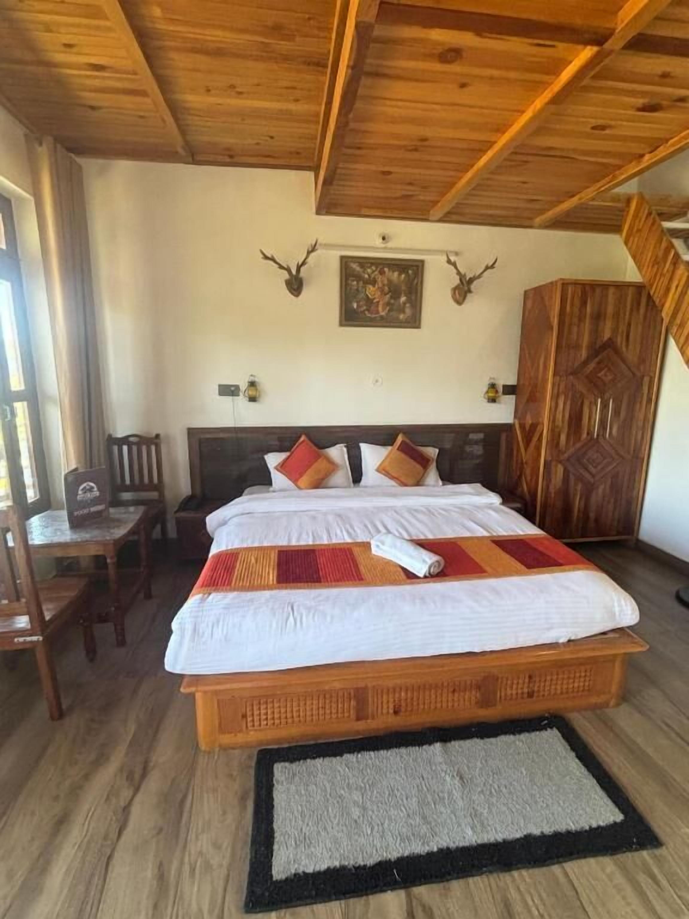 Ein Zimmer mit Holzboden, einem Bett mit gemustertem Überwurf, einem Holzschrank und einem gerahmten Bild an der Wand.