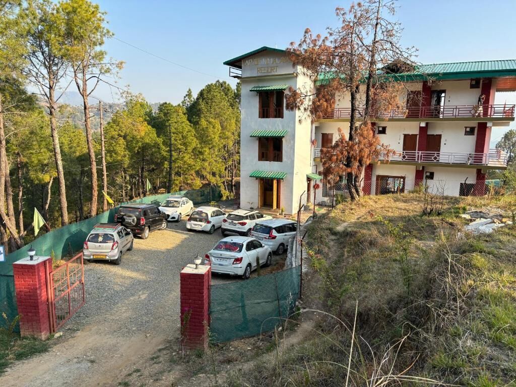 Un immeuble à plusieurs étages doté d’un toit végétalisé, un espace de stationnement avec plusieurs voitures et un paysage naturel environnant.