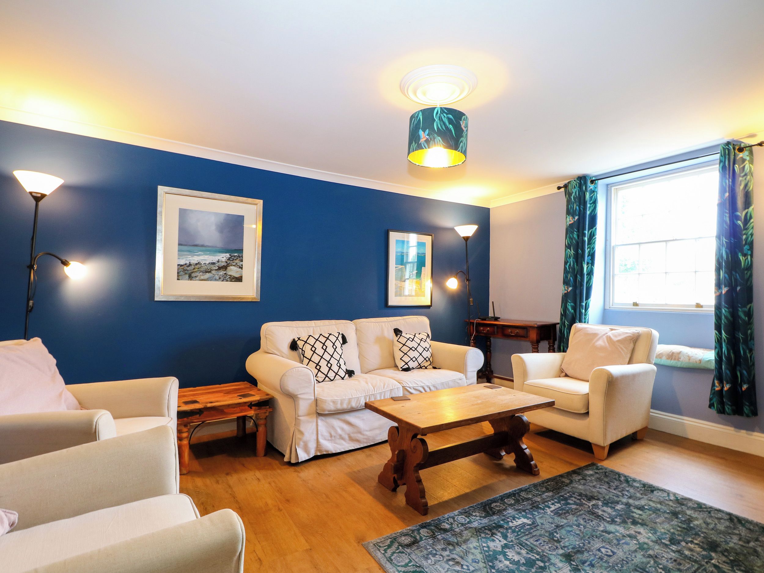 A living room with a blue wall, two white sofas, a wooden coffee table, and a patterned rug.