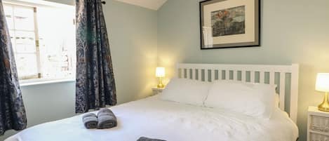 A bedroom with a bed, two bedside lamps, a framed picture on the wall, and a window with curtains.
