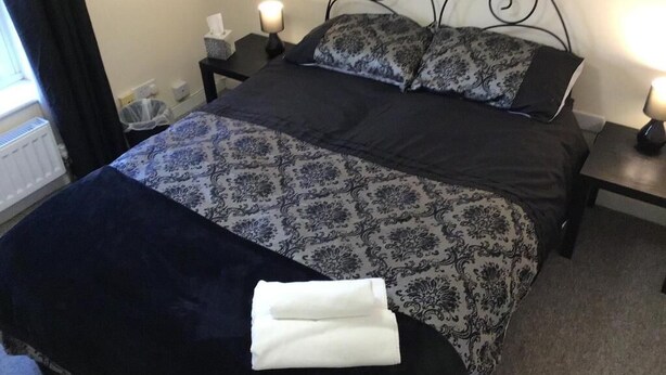 Una cama bien hecha con una colcha estampada, dos almohadas y una toalla blanca doblada en el reposapiés.