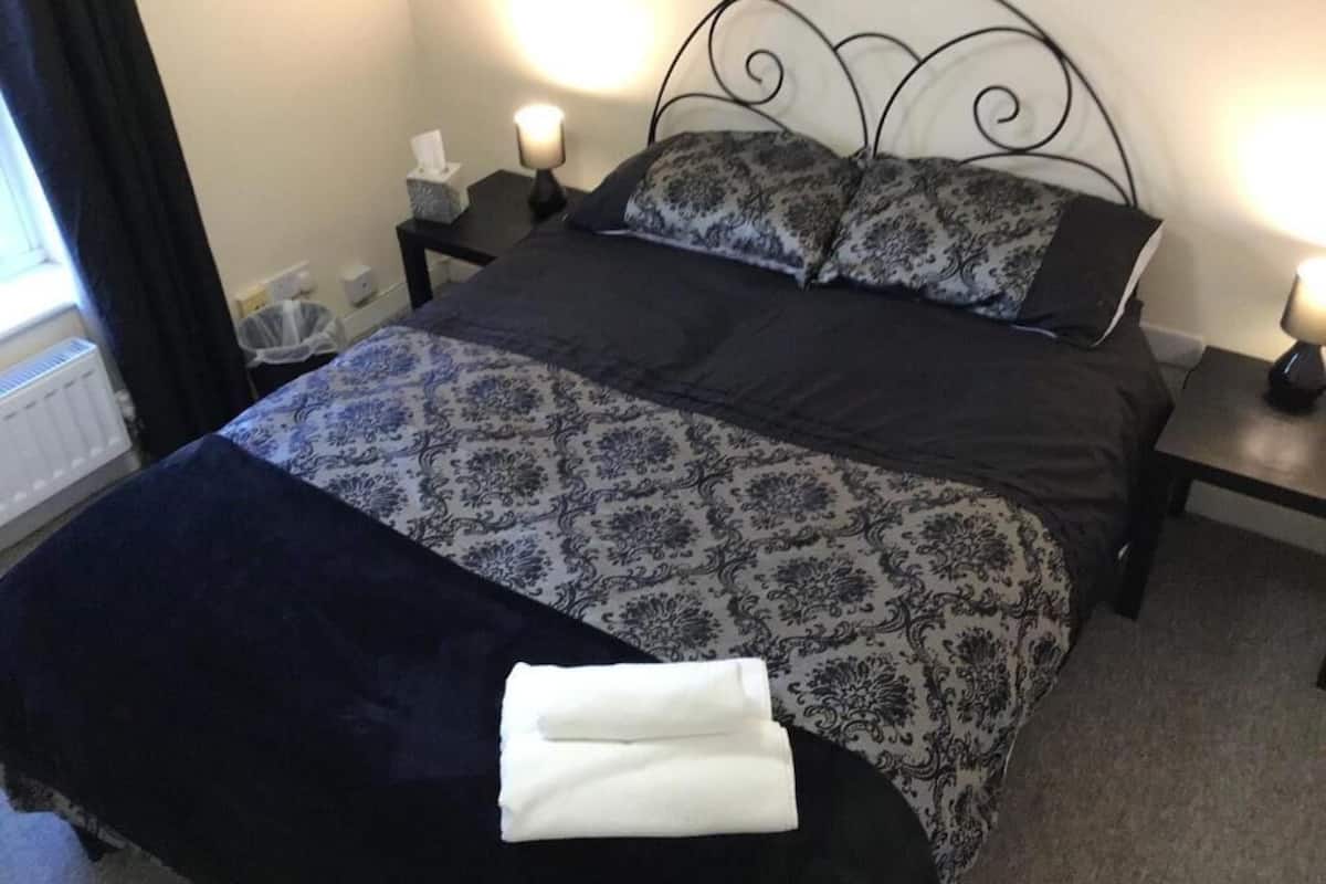 Una cama bien hecha con una colcha estampada, dos almohadas y una toalla blanca doblada en el reposapiés.