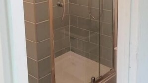 Una ducha con paredes de azulejos y una alfombra azul, protegida por cristales.