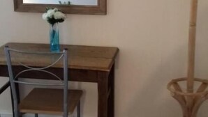 Una habitación con un escritorio de madera, una silla, un florero con flores, un perchero y un espejo grande en la pared.