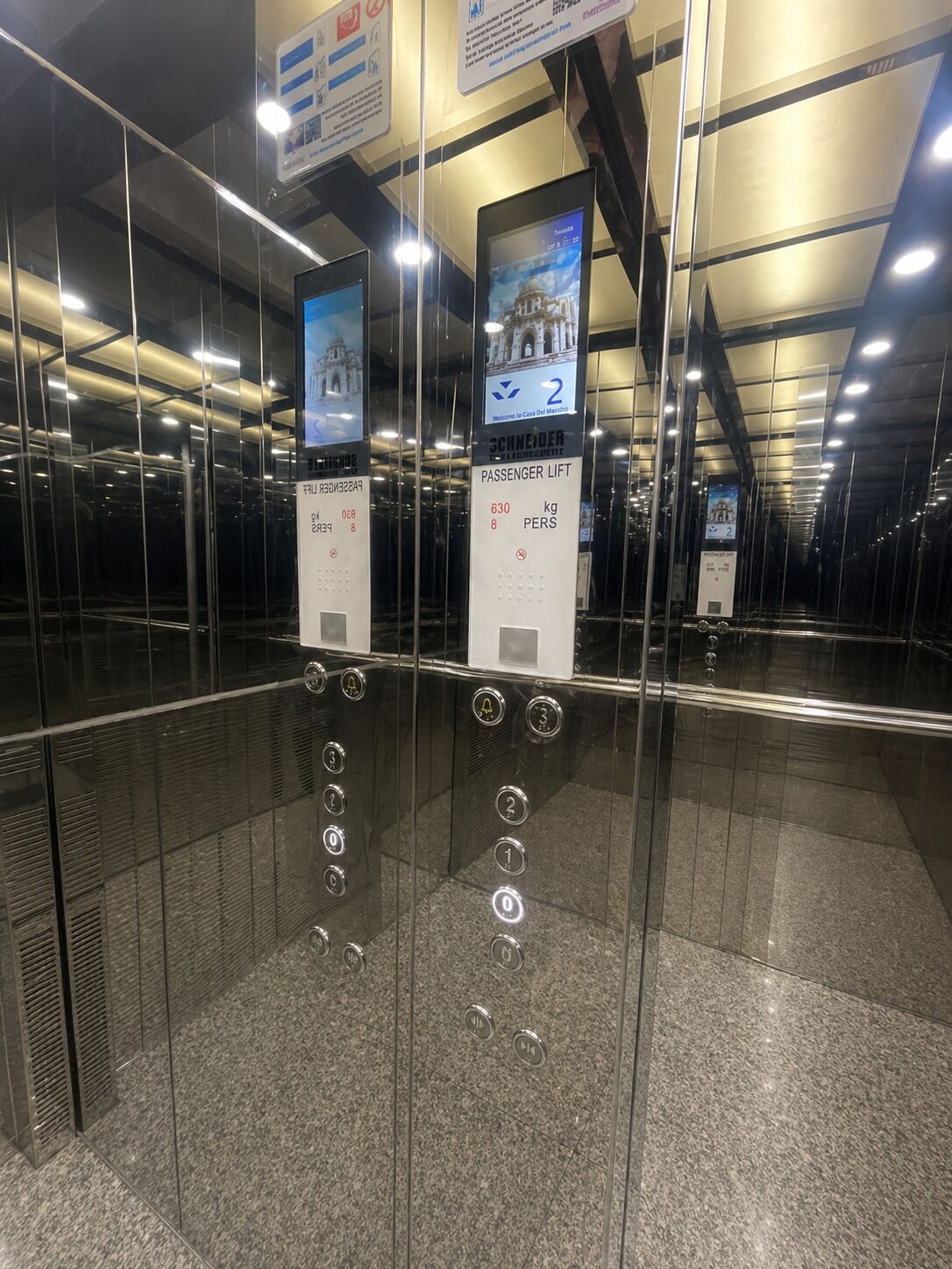 An elevator interior with glass walls, digital displays, and floor indicators.